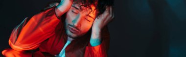 curly and stylish man with closed eyes posing in orange shirt on blue, banner