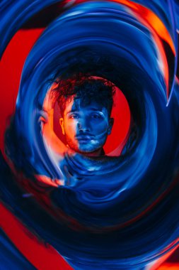 curly man looking at camera through futuristic circle on red and blue background 