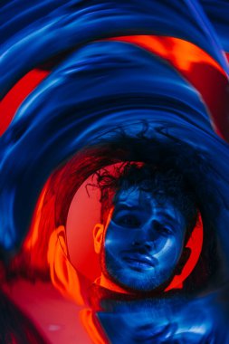 curly man looking at camera through futuristic neon blue and red circle 