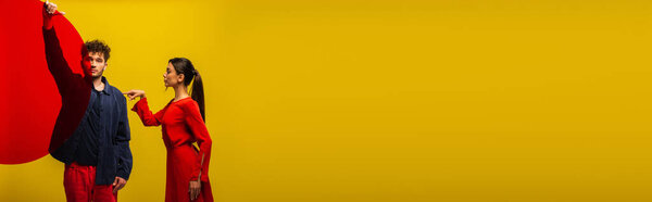 модный кудрявый мужчина держит круглую форму стекла рядом с женщиной изолированы на желтый, баннер