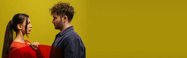 side view of trendy and young models posing near round shape glass isolated on green, banner