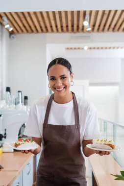 Positive african american seller holding dessert and looking at camera in sweet shop 