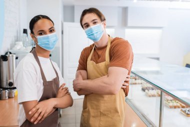 Tıbbi maskeli ırklar arası satıcılar şekerleme dükkanında kollarını kavuşturuyorlar. 