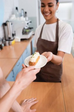 Smiling african american saleswoman giving dessert to colleague in sweet shop 