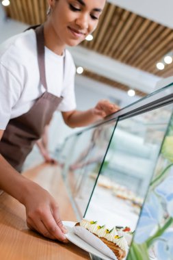 Bulanık Afrikalı Amerikalı satıcı şeker dükkanında eclair 'i vitrininden alıyor. 