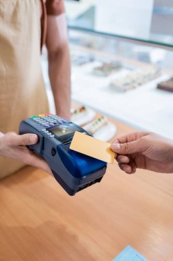 Cropped view of african american customer paying with credit card near seller in sweet shop 