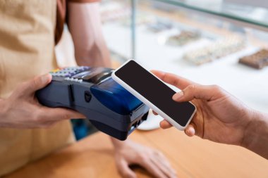 Cropped view of african american client paying with smartphone near seller in sweet shop 
