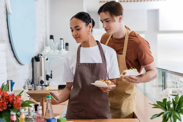 Interracial Sellers Aprons Holding Dessert Using Digital Tablet Confectionery — Photo