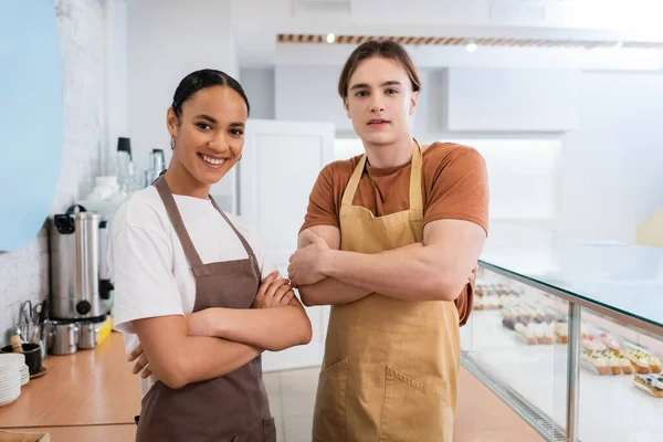 Smiling Interracial Sellers Aprons Crossing Arms Sweet Shop — Stock Photo, Image
