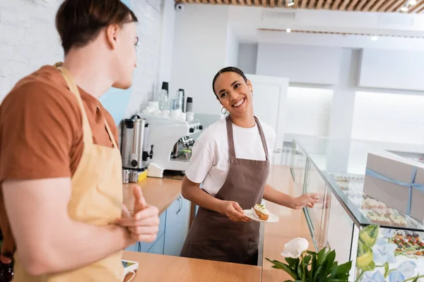 Smiling African American Seller Holding Dessert Showcase Blurred Colleague Sweet — Stock Photo, Image