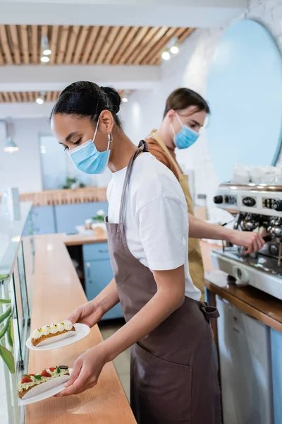 African American Seller Medical Mask Holding Eclairs Showcase Confectionery — Stock Photo, Image