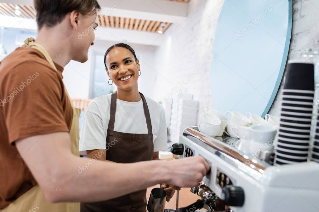 Smiling african american seller looking at barista making coffee in confectionery 