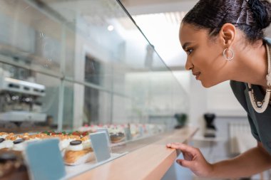 Side view of african american client looking at eclairs in showcase in confectionery 