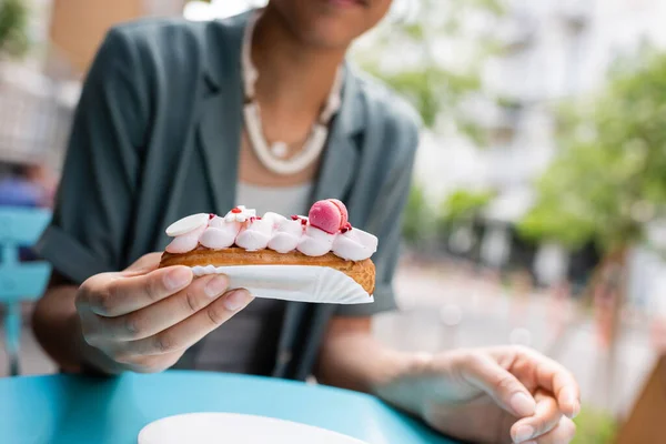 Cropped View Blurred African American Woman Holding Delicious Eclair Terrace — стоковое фото