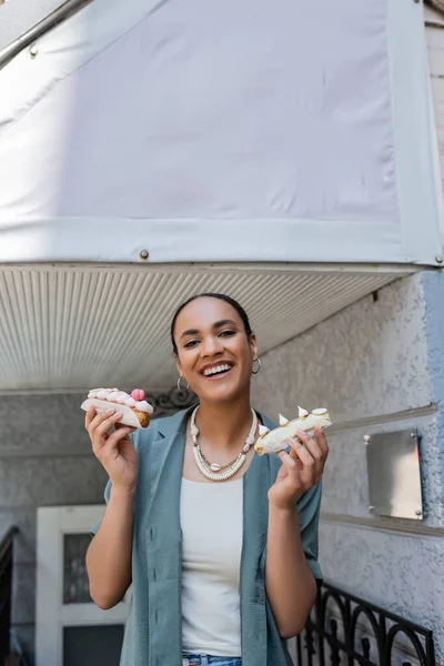 Happy African American Woman Holding Tasty Eclairs Sweet Shop Outdoors — Foto de Stock