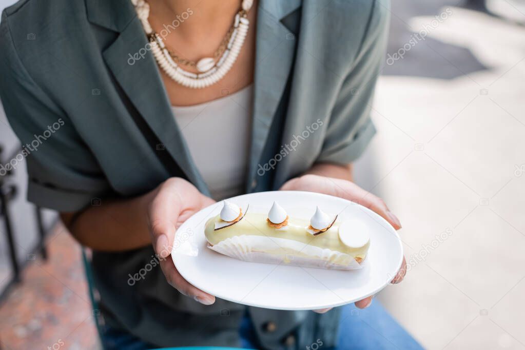 Cropped view of african american customer holding tasty eclair on terrace of confectionery 