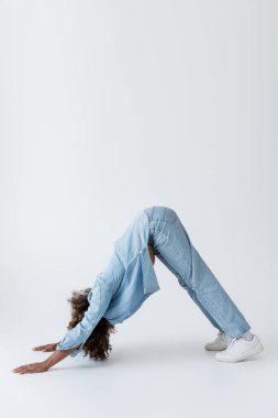 side view of african american woman in denim clothes standing in dolphin pose on grey background