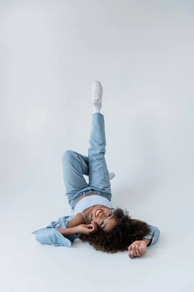 Smiling African American Woman Lying Back Raised Legs Grey Background — Stock Fotó