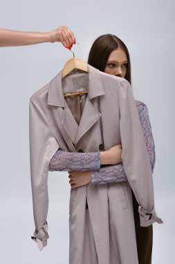 teenage model hugging stylish trench coat while woman holding hanger isolated on grey