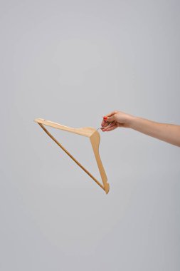 cropped view of woman holding wooden hanger isolated on grey