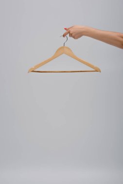 partial view of woman holding wooden hanger isolated on gray