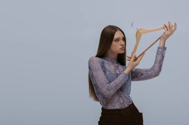 brunette teenage model holding wooden hanger isolated on grey