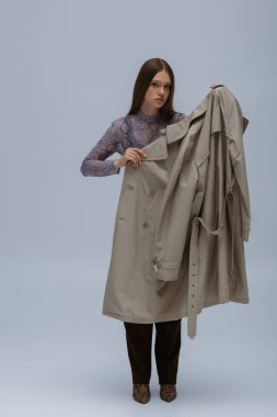 brunette teenage girl posing with trendy trench coat isolated on grey 