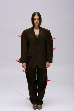 full length of teenage girl in brown stylish suit pinned with clothespins on rope posing on grey 
