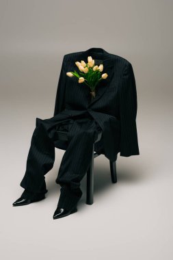 blooming tulips and blue stylish suit hanging on chair on grey
