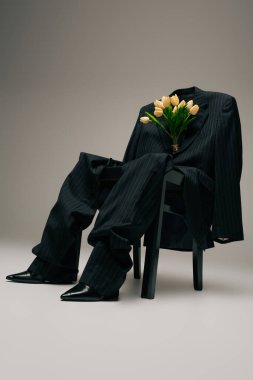 blooming bouquet of tulips and blue stylish suit hanging on chair on grey