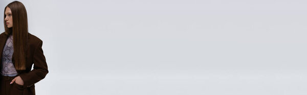 красивая модель-подросток в коричневом высококачественном костюме, позирующая с рукой в кармане, изолированная на сером, баннере