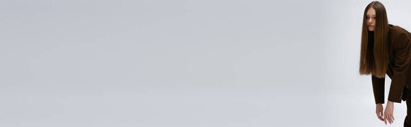 красивая модель подростка в коричневом высококачественном костюме, позирующем изолированно на сером, баннере