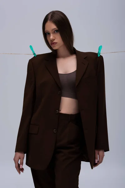 stylish teenage girl in brown blazer pinned with clothespins on rope isolated on grey