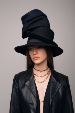 brunette model in leather jacket and different black hats on head isolated on grey
