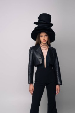 teenage model in leather jacket and different black hats on head isolated on grey
