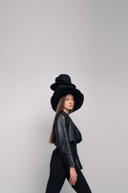 brunette model in leather jacket and black hats on head isolated on grey