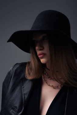 teenage model in black floppy hat and stylish leather jacket isolated on grey