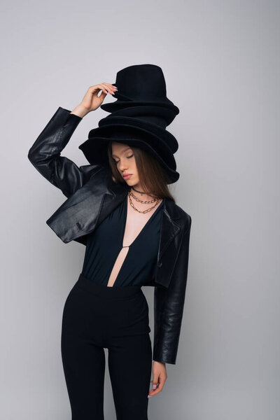 brunette model in leather jacket holding derby hat isolated on grey