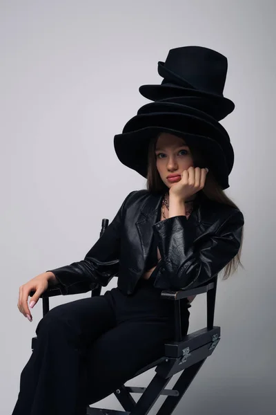 Брюнетка Модель Кожаной Куртке Различные Черные Шляпы Сидя Стуле Изолированы — стоковое фото