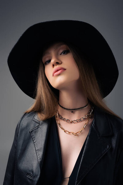 модель подростка в мягкой шляпе и черной кожаной куртке, изолированной на сером