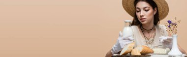 Stylish woman in gloves touching bottle of milk near butter and bread isolated on beige, banner 