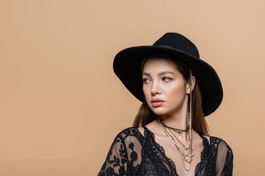Trendy young woman in black hat looking away isolated on beige 