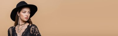 Brunette woman in black hat looking away isolated on beige, banner 