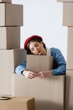 Fashionable woman in beret and eyeglasses standing near cardboard boxes isolated on white 