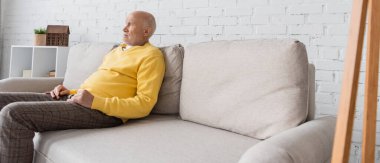 Side view of pensioner sitting on couch at home, banner 