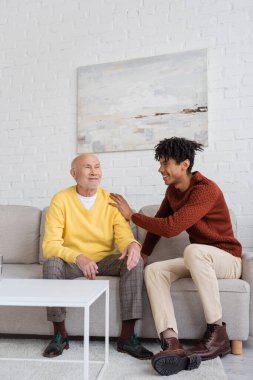 Happy african american grandson hugging grandparent on couch at home 