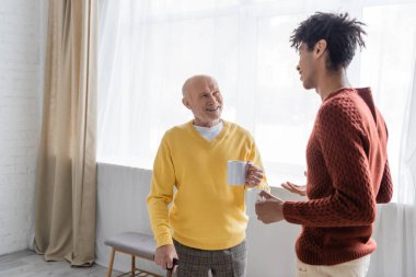 Interracial granddad and grandson holding cups of tea at home 