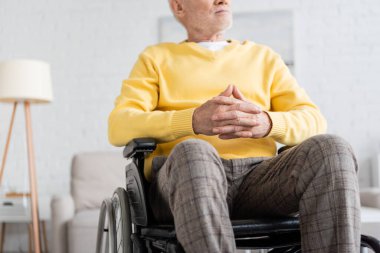 Cropped view of pensioner sitting in wheelchair at home 