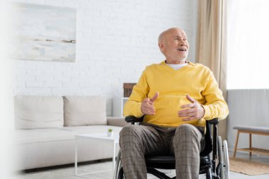 Positive elderly man looking away while sitting in wheelchair at home 