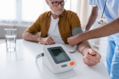 Tonometer near blurred african american nurse and patient at home 